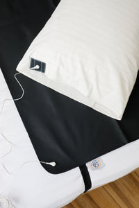 Taie d'oreiller Earthle sur un lit à côté du tapis de sommeil noir, avec le câble de mise à la terre