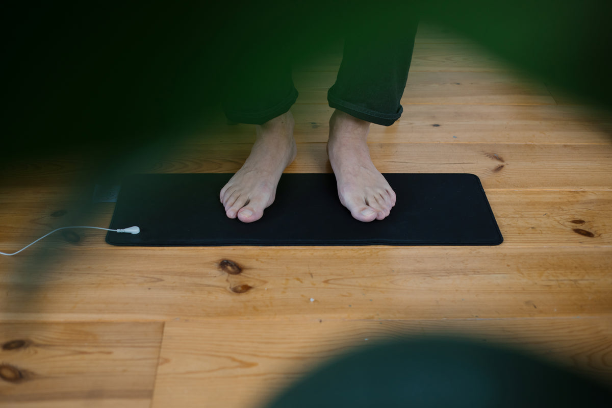 Pieds nus sur le tapis de mise à la terre Earthle posé au sol, utilisé comme repose-pieds