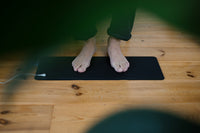 Pieds nus sur le tapis de mise à la terre Earthle posé au sol, utilisé comme repose-pieds