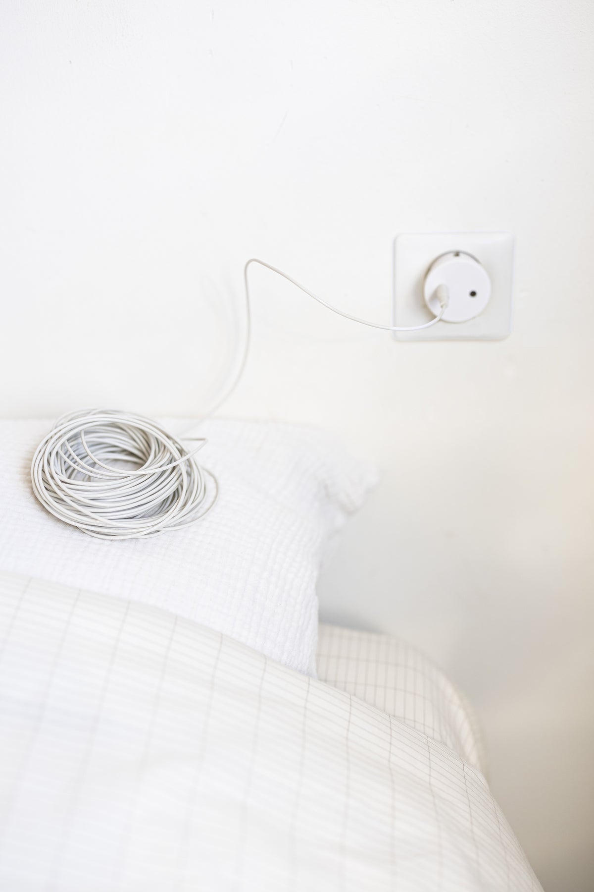 Earthle aardingsverlengsnoer opgerold op een bed, met de kabel naar het stopcontact aan de muur