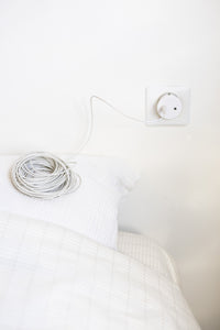 Earthle aardingsverlengsnoer opgerold op een bed, met de kabel naar het stopcontact aan de muur
