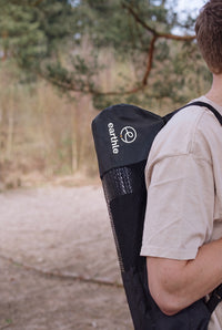 Iemand draagt de Earthle aardingsyogamat in de draagtas op de rug, buiten in het bos