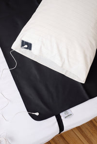 Taie d'oreiller de mise à la terre Earthle sur un lit à côté du tapis de sommeil de mise à la terre noir, avec le câble de mise à la terre